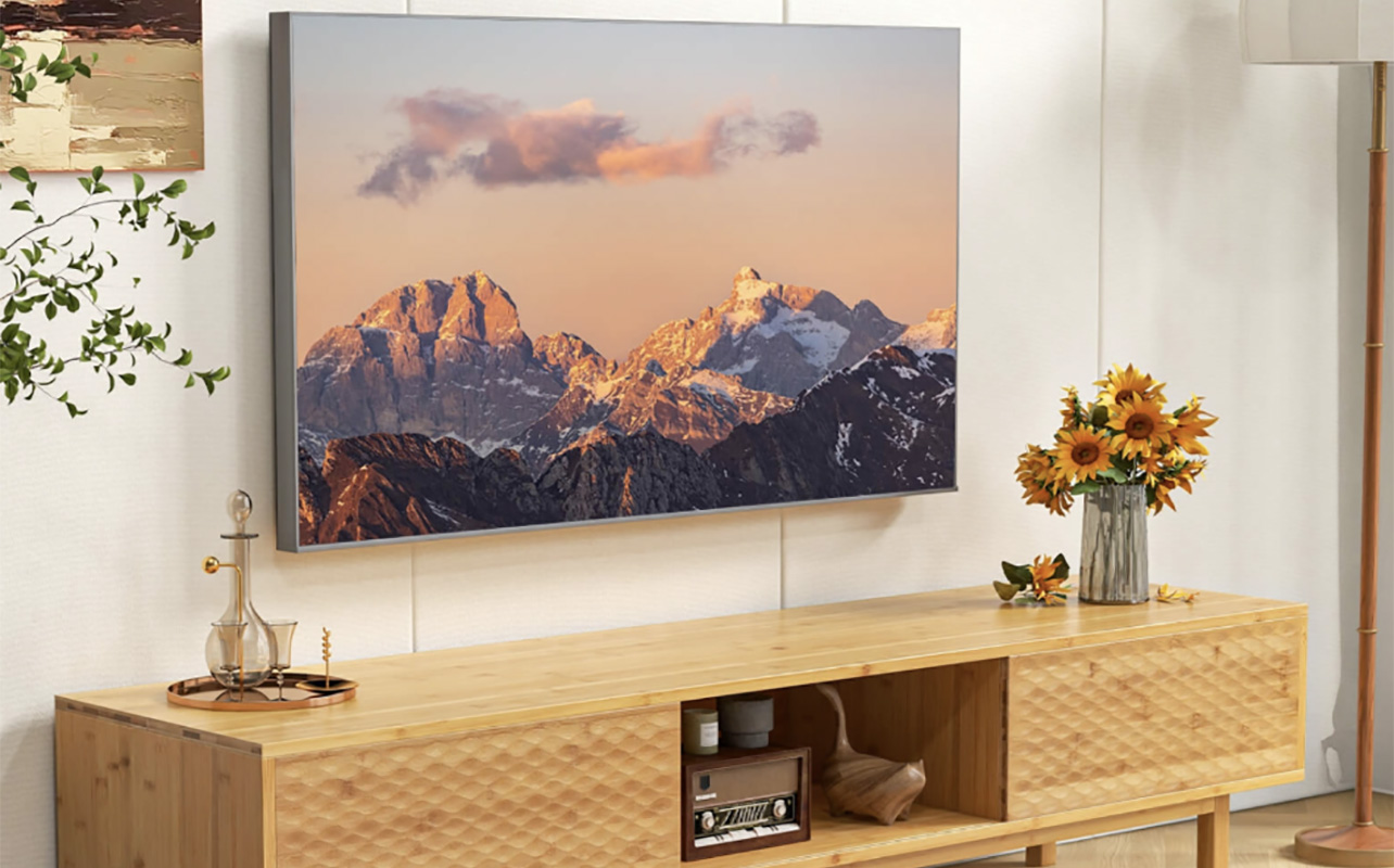 A TV mounted on the wall under a Costeay bamboo TV stand.